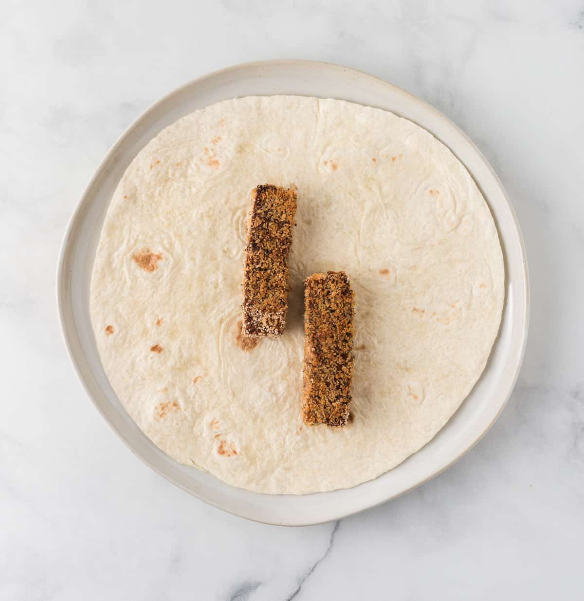 a flour tortilla with two tofu strips on it