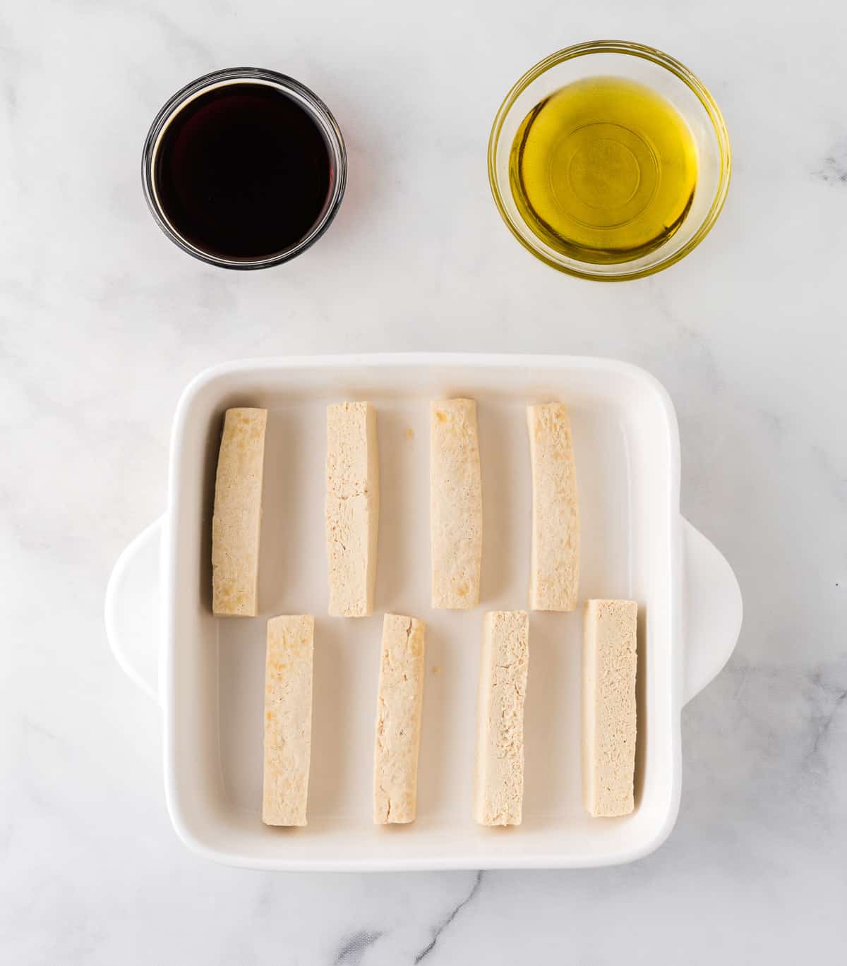 tofu blocks in a baking dish next to soy sauce and olive oil