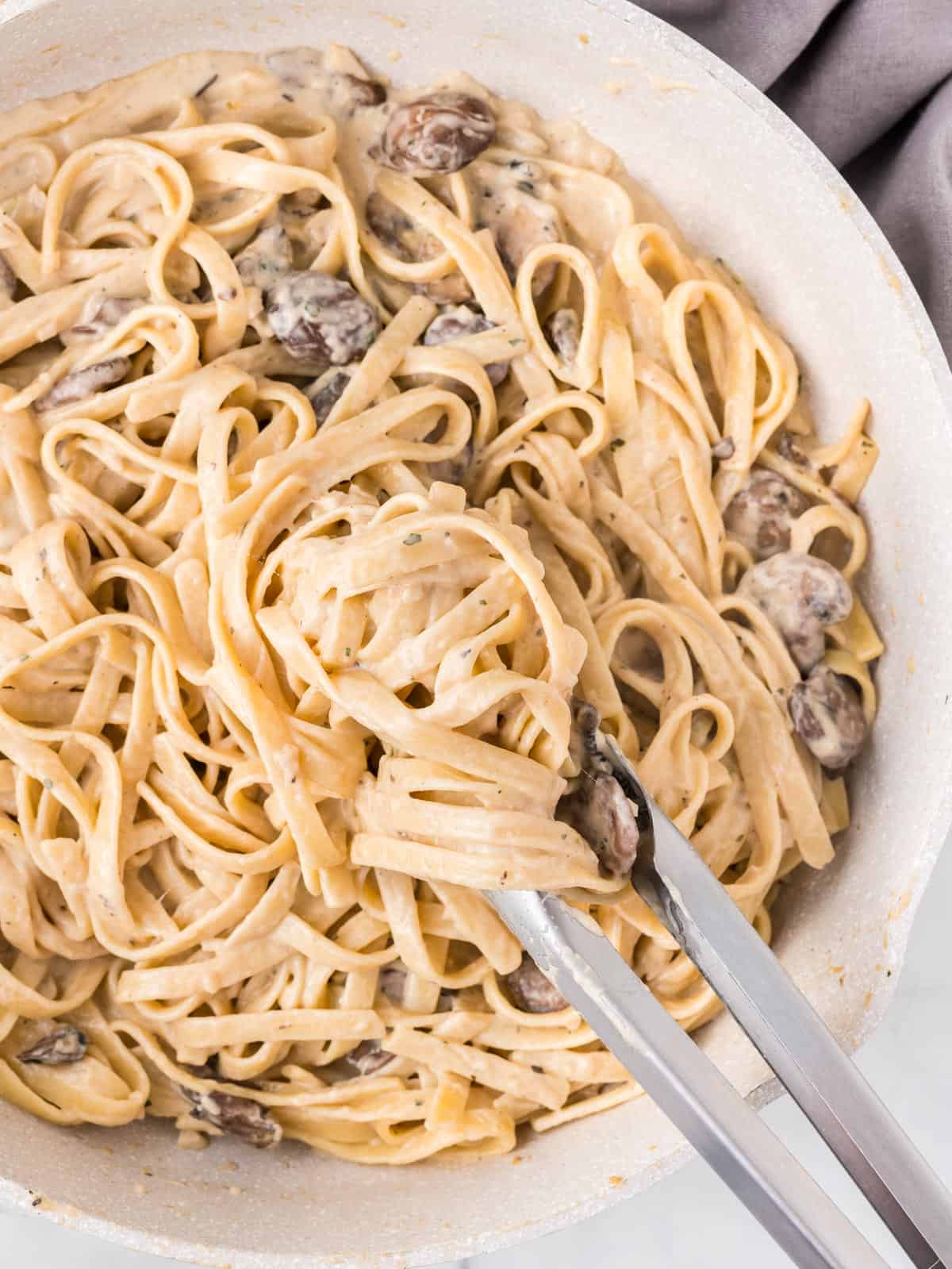 tongs taking a scoop of mushroom pasta from the skillet