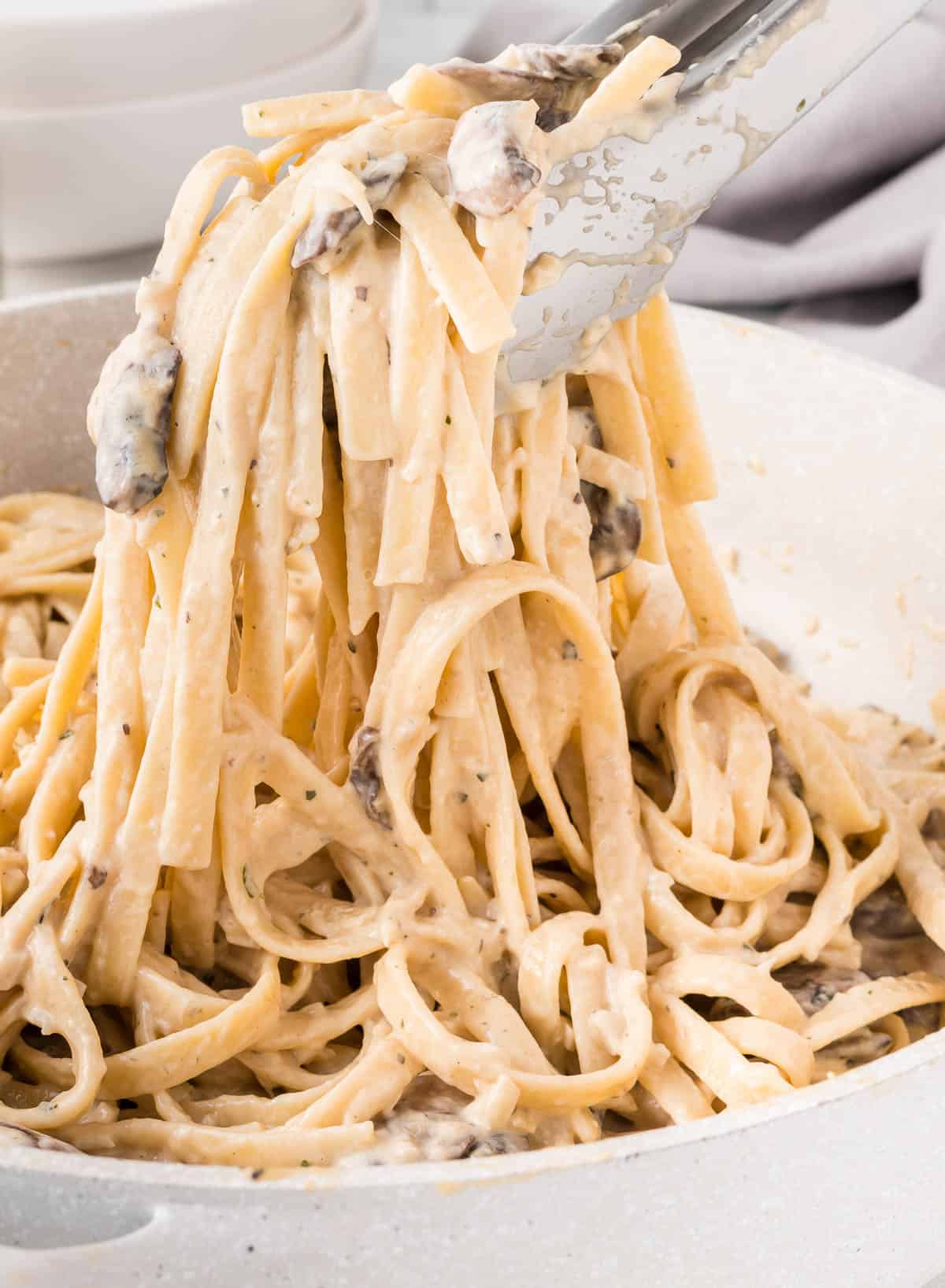 tongs taking a scoop of mushroom pasta from the skillet