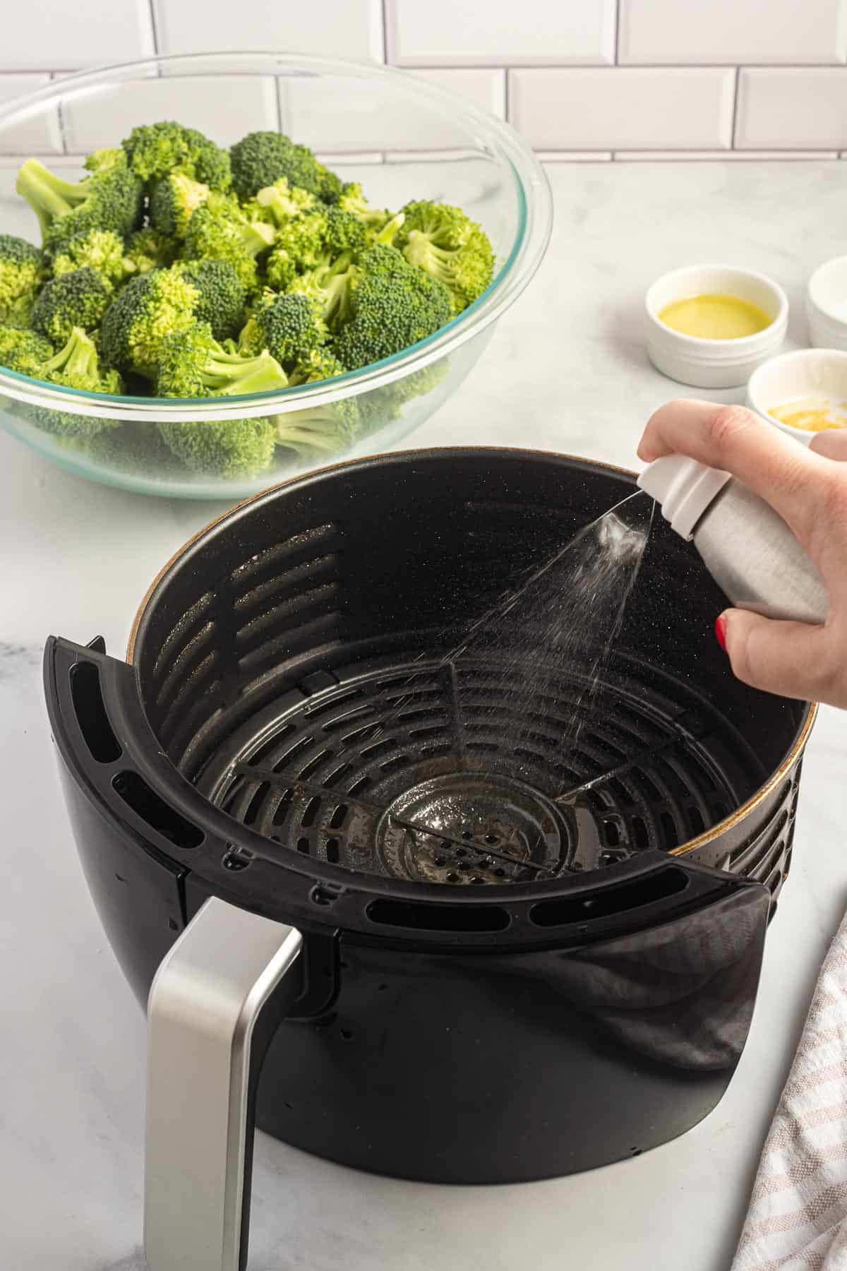 spraying olive oil spray into an air fryer basket