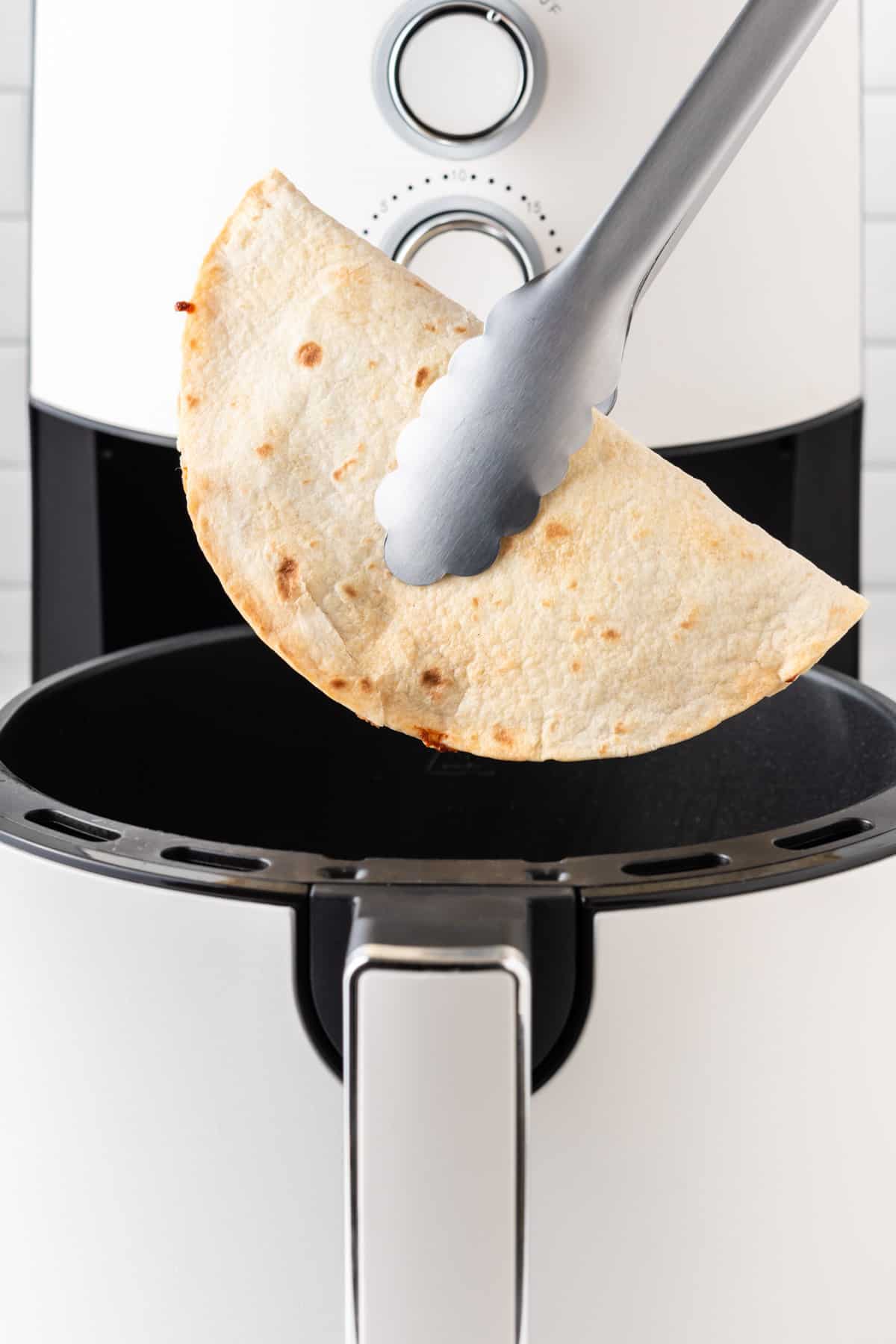 tongs removing the quesadilla from the air fryer