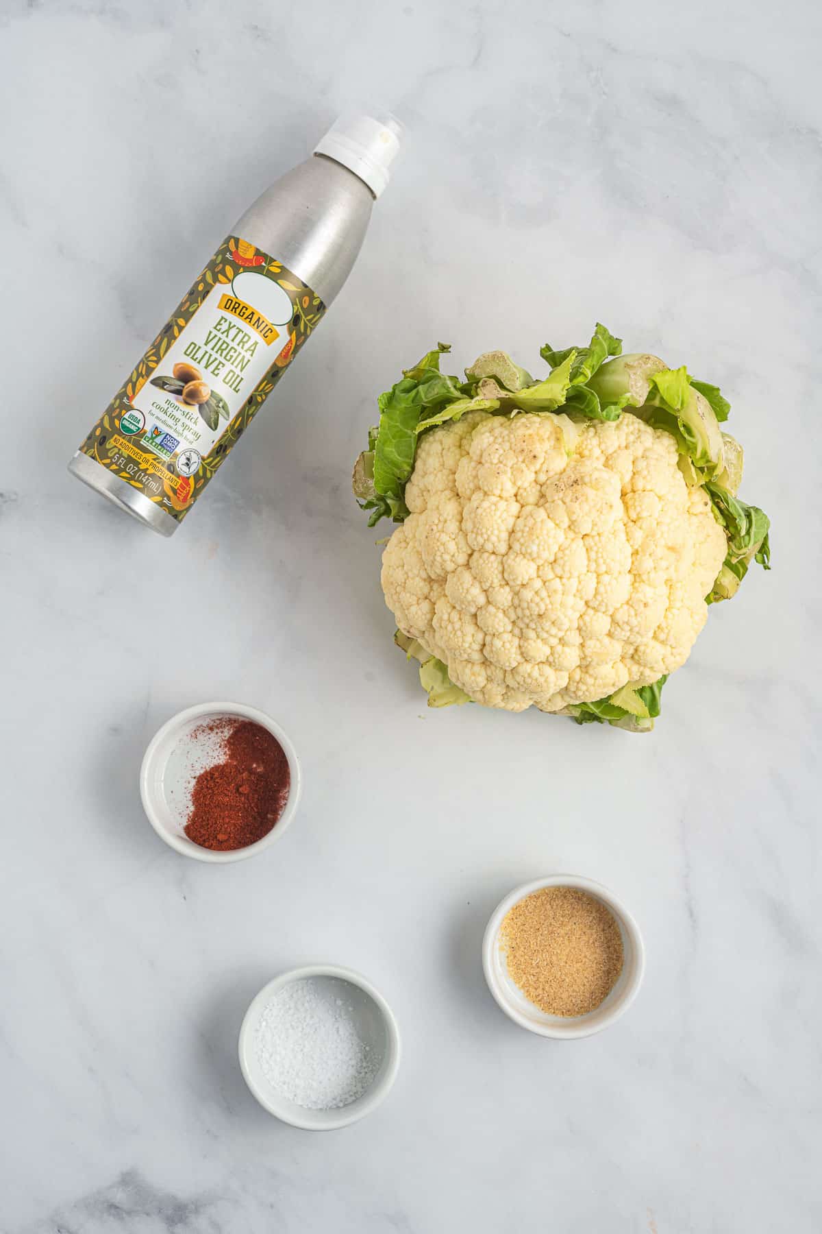 a head of cauliflower next to spices and spray olive oil