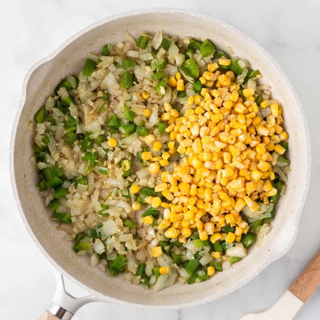 adding frozen corn to the vegetables in the skillet