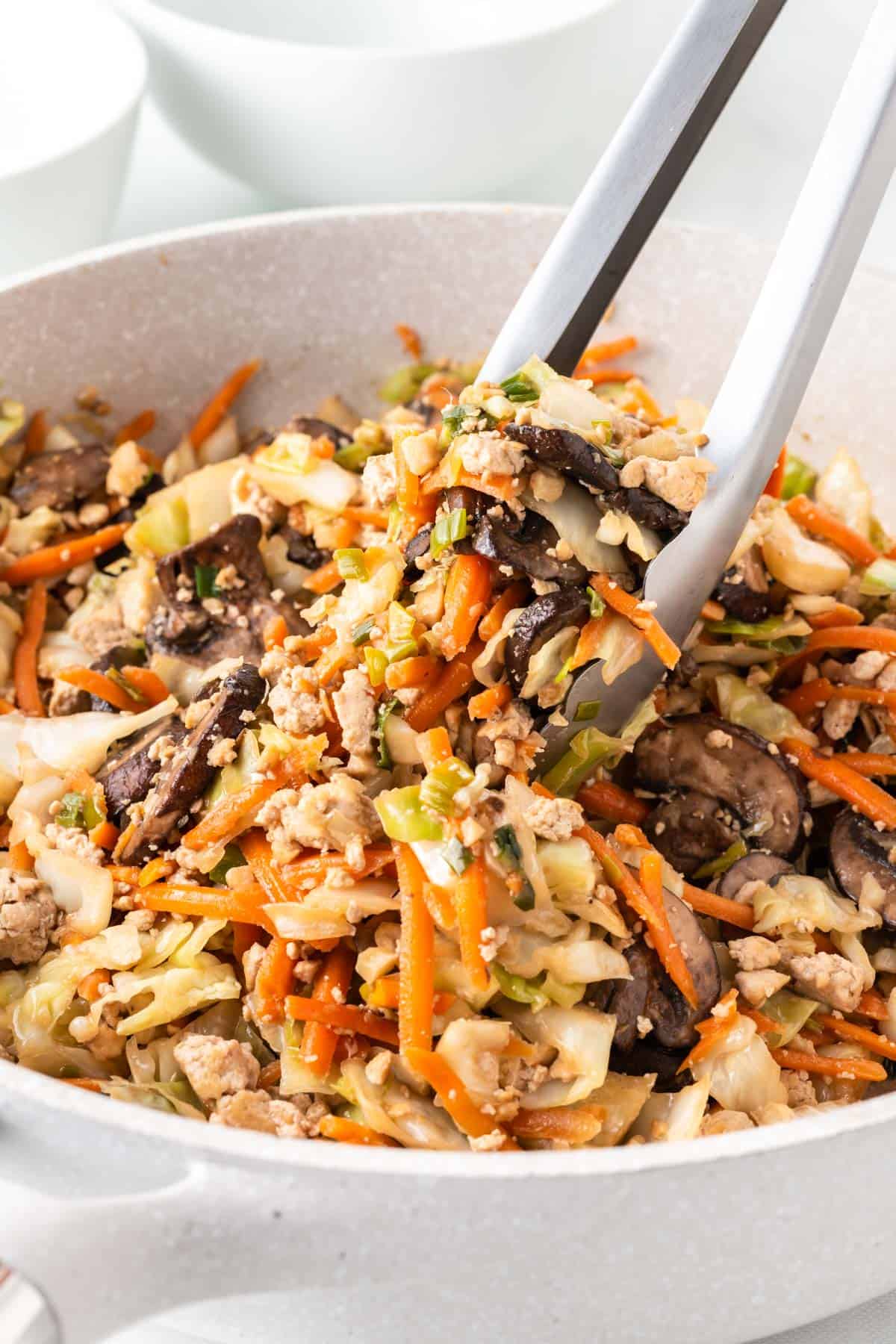 tongs taking egg roll filling from the skillet