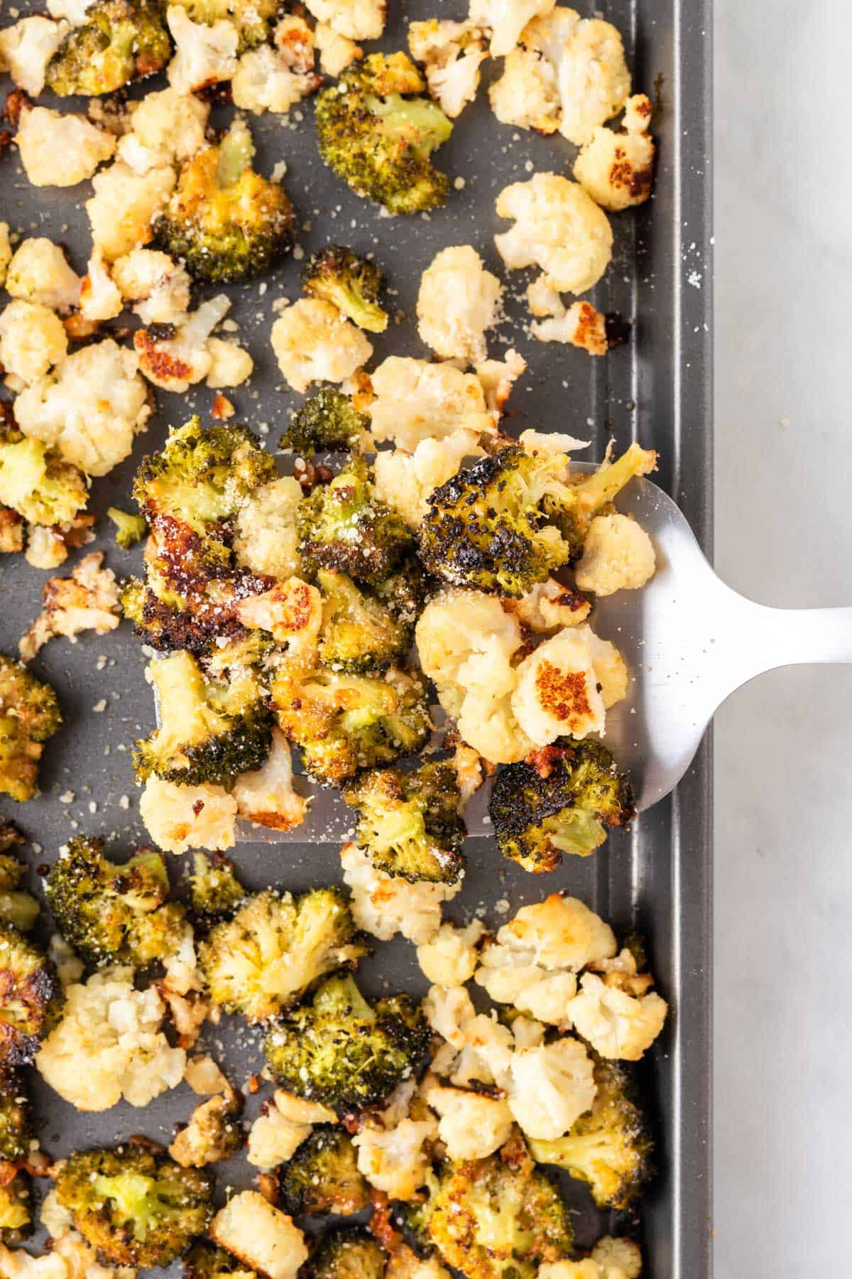 spatula taking roasted broccoli and cauliflower from the pan