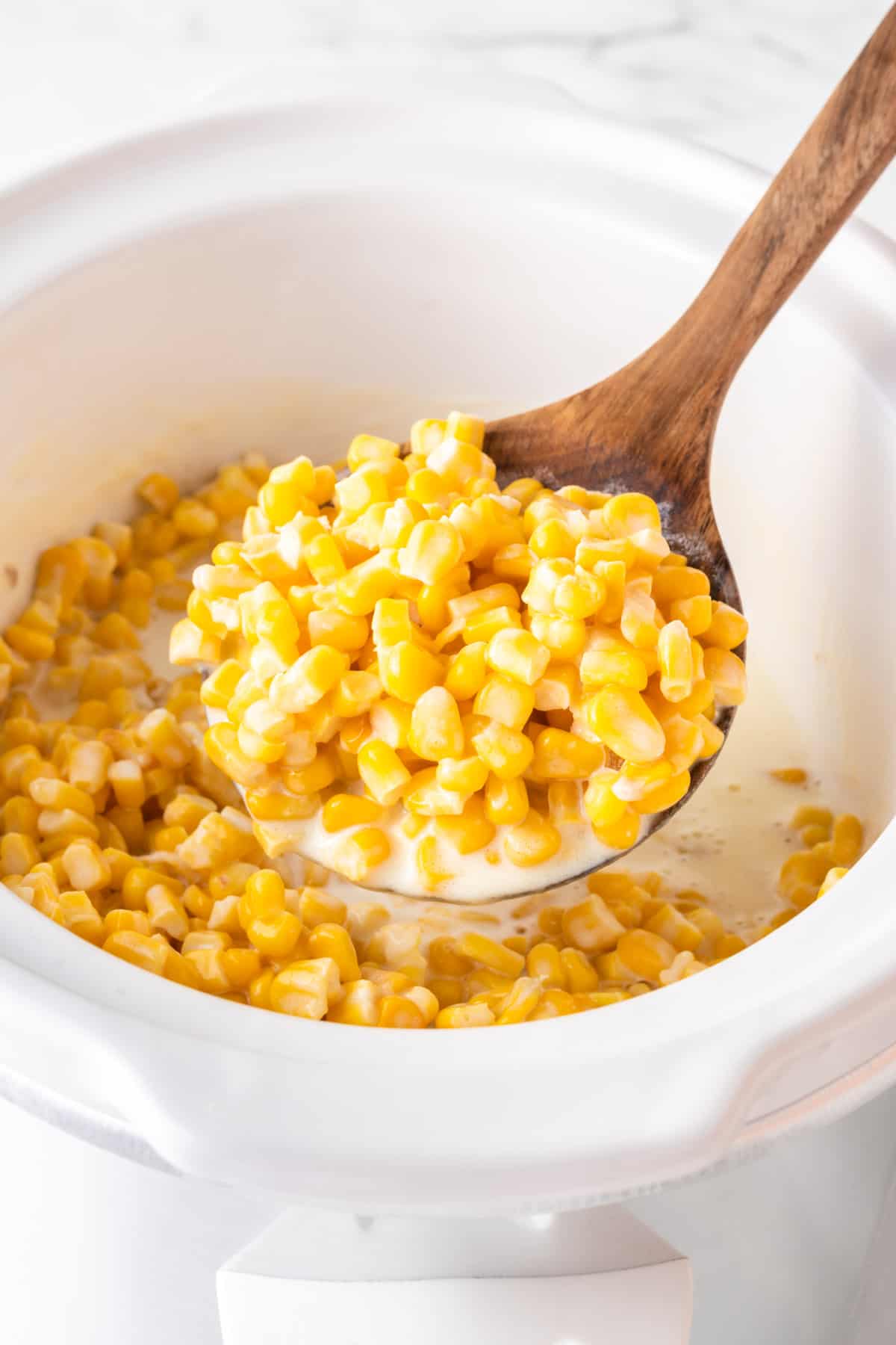 wooden spoon taking creamed corn from the slow cooker