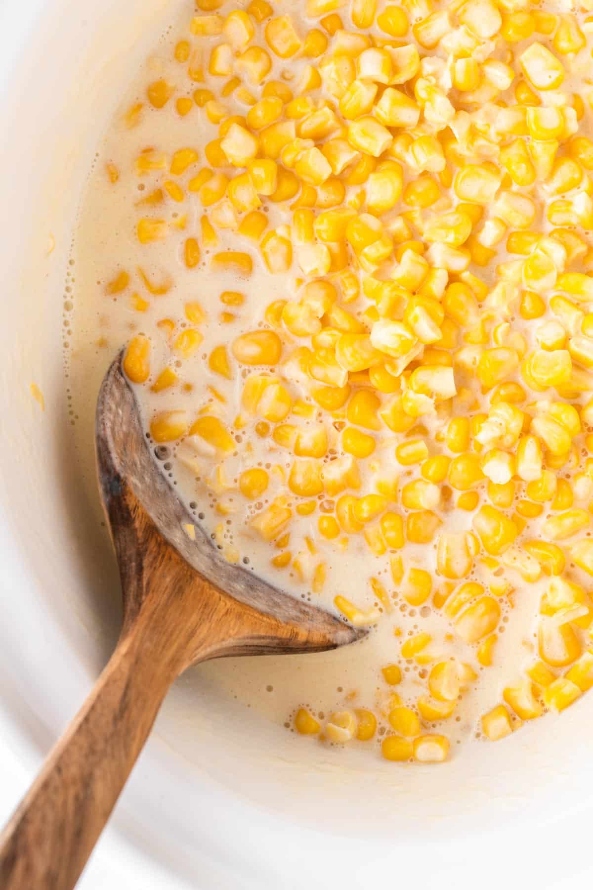 wooden spoon taking creamed corn from the slow cooker