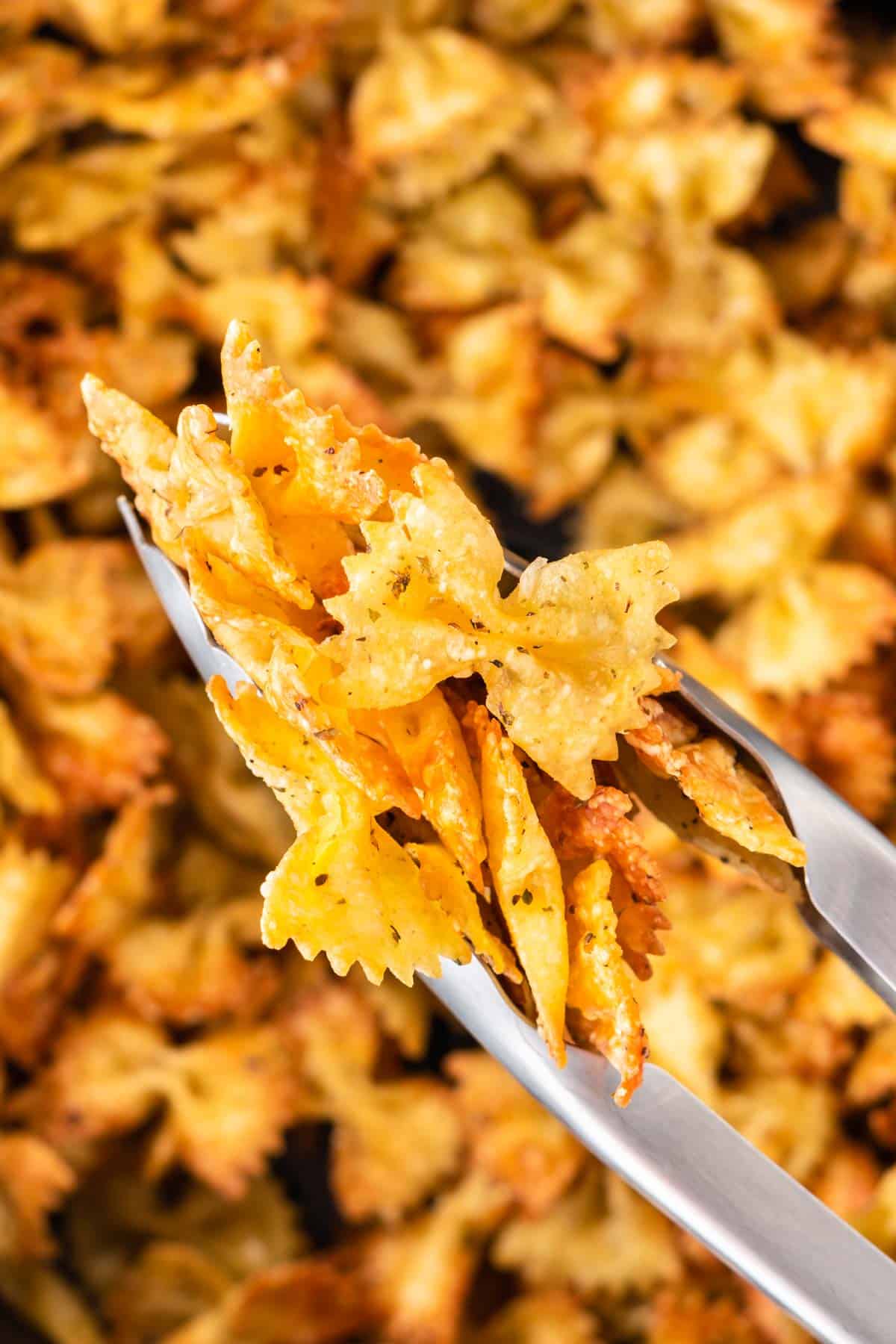 tongs taking pasta chips from the air fryer