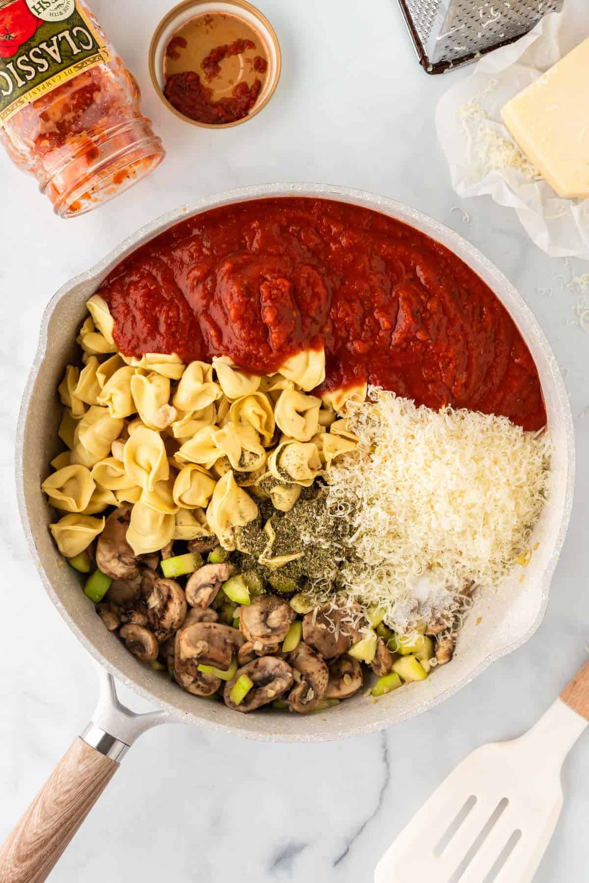 adding sauce, cheese, spices, and tortellini to the skillet