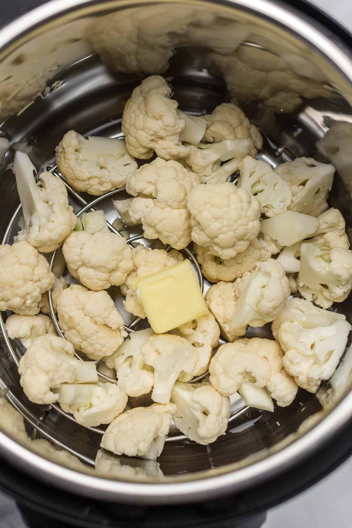 cauliflower florets inside an instant pot with a pat of butter on top