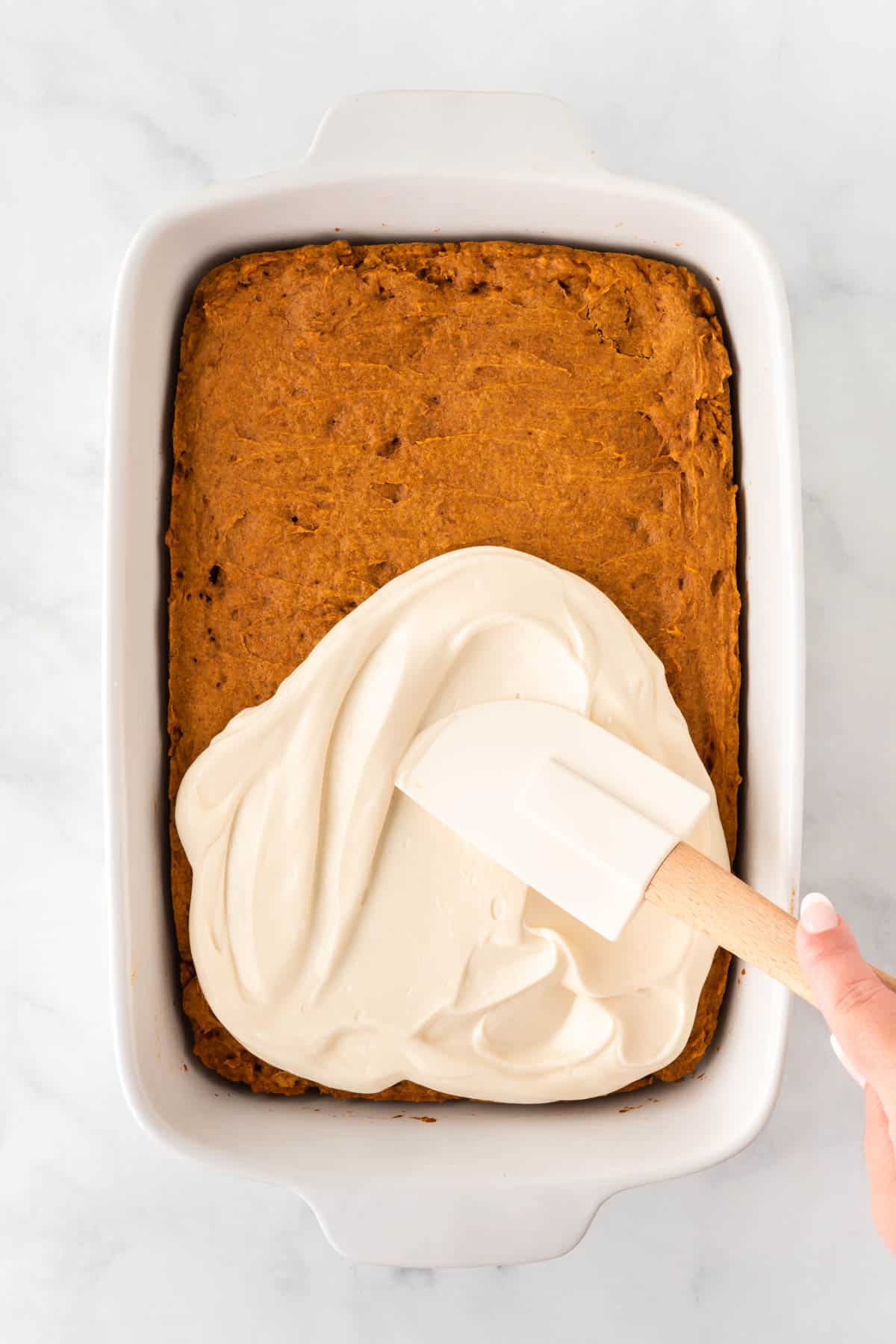 spreading cream cheese frosting over the pumpkin bars