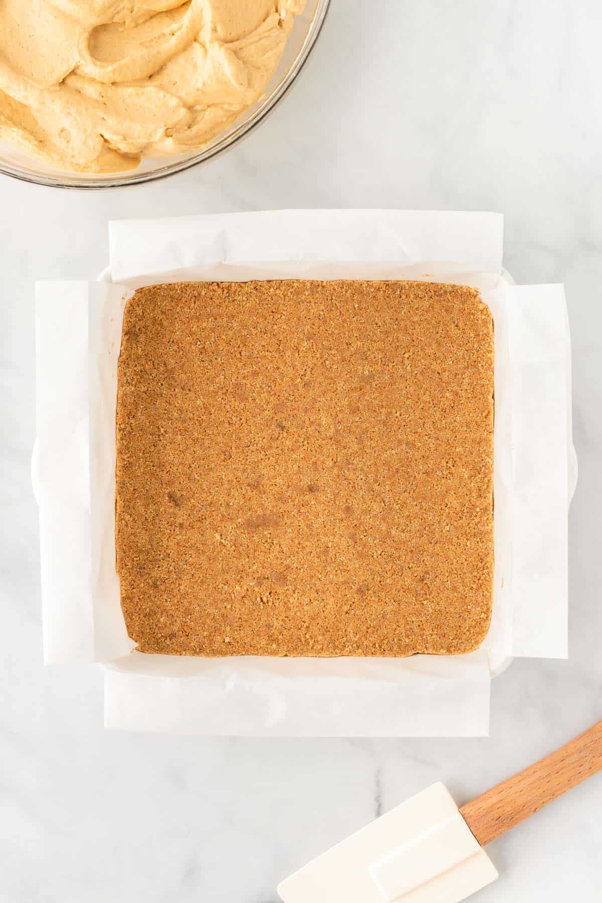 graham cracker crust pressed down into an 8 by 8 baking dish lined with parchment paper