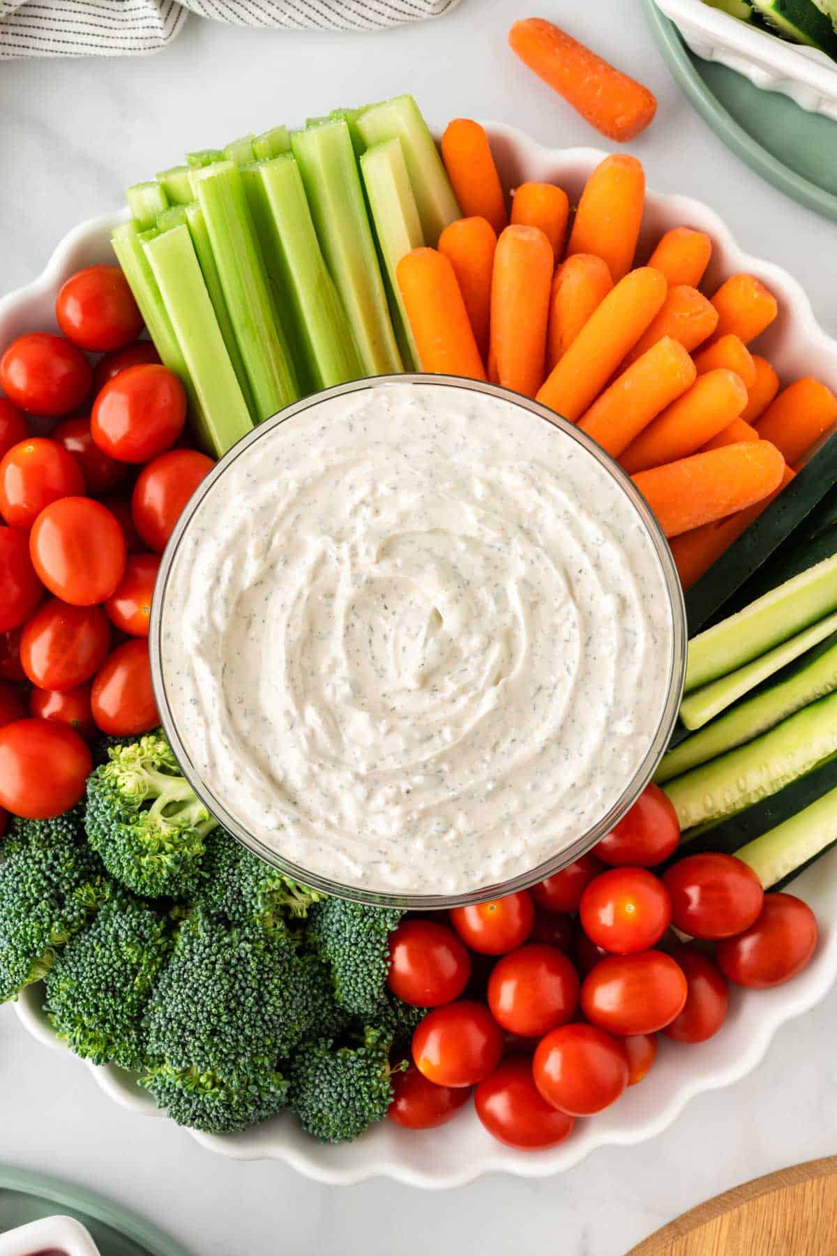 dip in a bowl surrounded with broccoli, cherry tomatoes, celery, and baby carrots