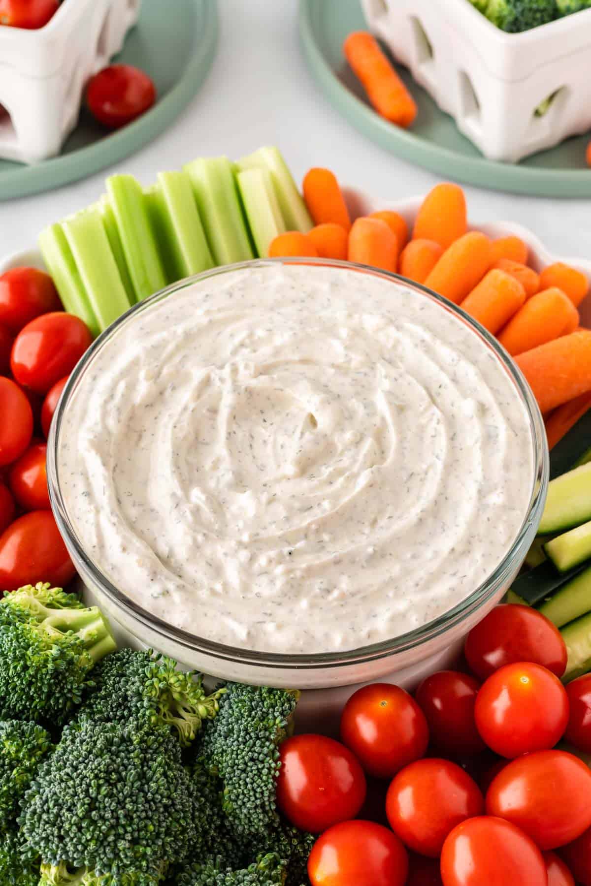 dip in a bowl surrounded with broccoli, cherry tomatoes, celery, and baby carrots