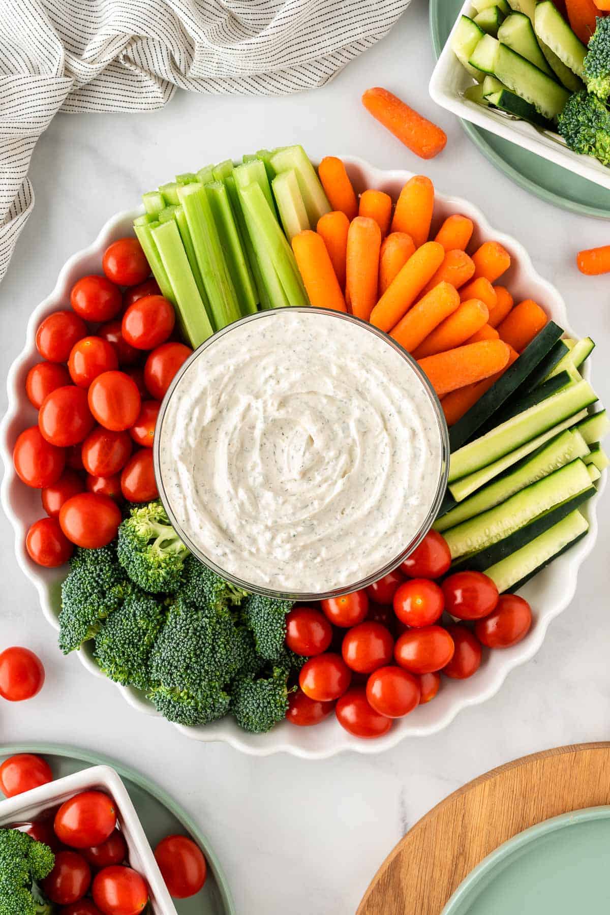 dip in a bowl surrounded with broccoli, cherry tomatoes, celery, and baby carrots