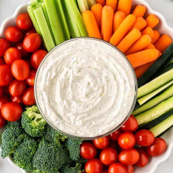 dip in a bowl surrounded with broccoli, cherry tomatoes, celery, and baby carrots