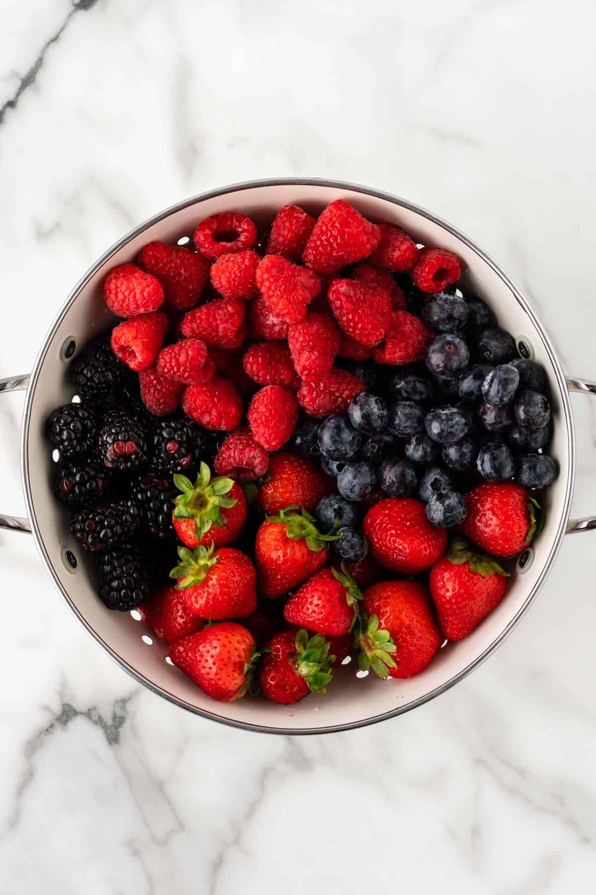 raspberries, blackberries, blueberries, and strawberries in a strainer