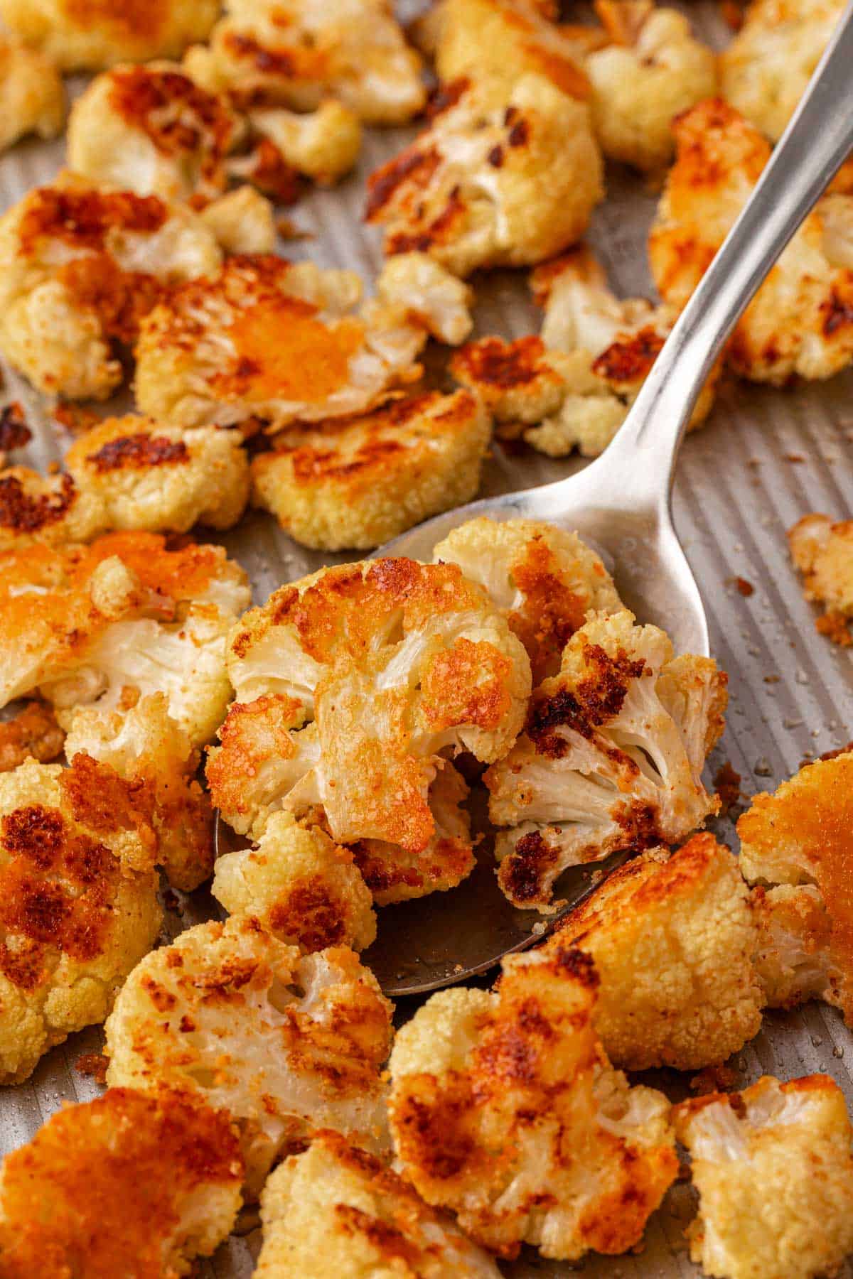 scooping parmesan roasted cauliflower from a baking sheet