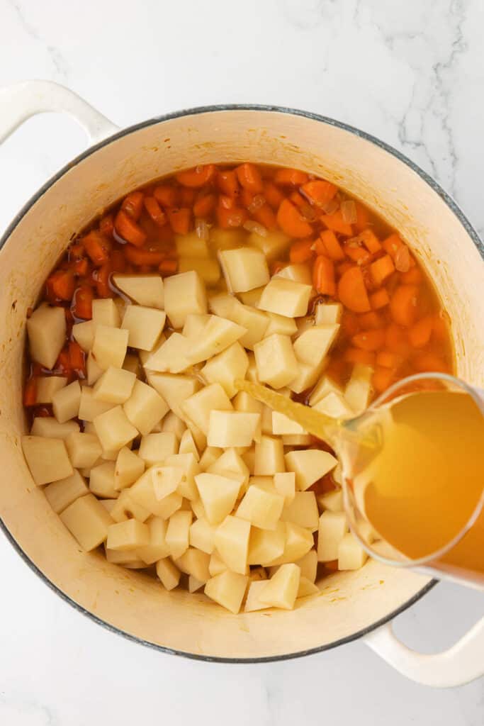 pouring vegetable broth over the potatoes and carrots