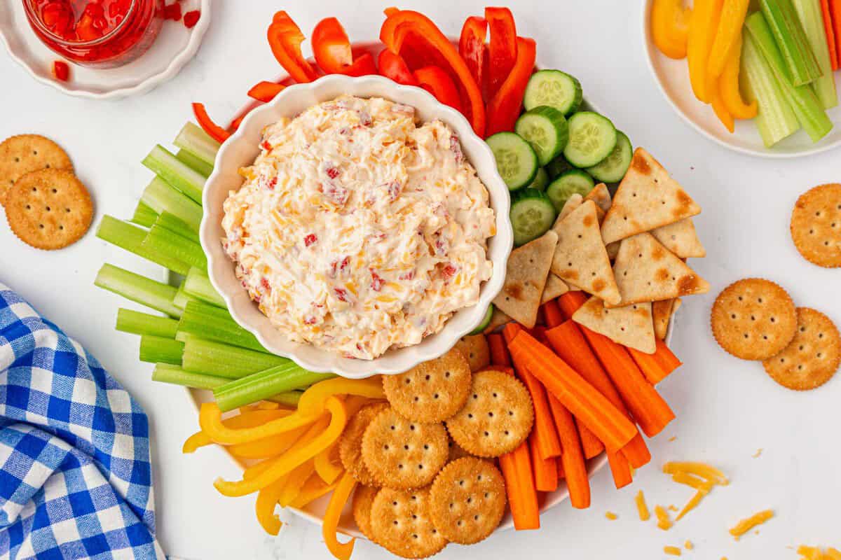 pimento cheese on a platter with crackers and cut up vegetables