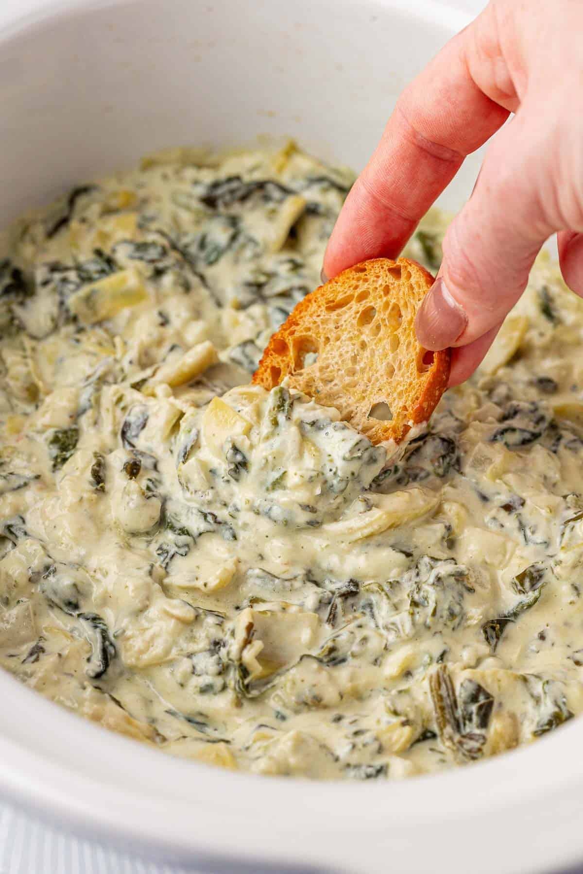 dipping a baguette slice into spinach artichoke dip