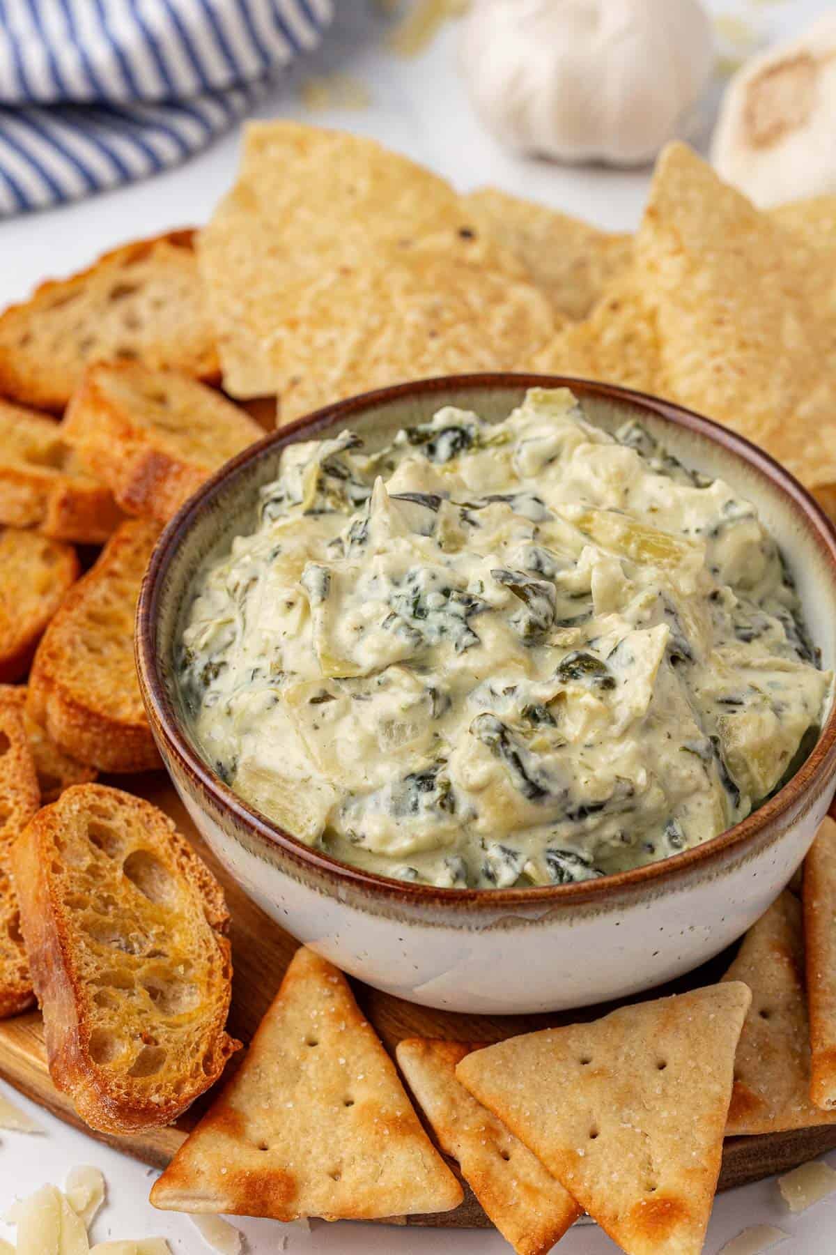 bowl of spinach artichoke dip with a plate of chips and crackers
