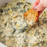 dipping a baguette slice into spinach artichoke dip
