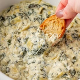dipping a baguette slice into spinach artichoke dip