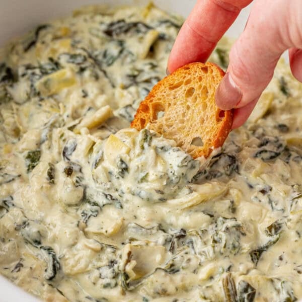 dipping a baguette slice into spinach artichoke dip