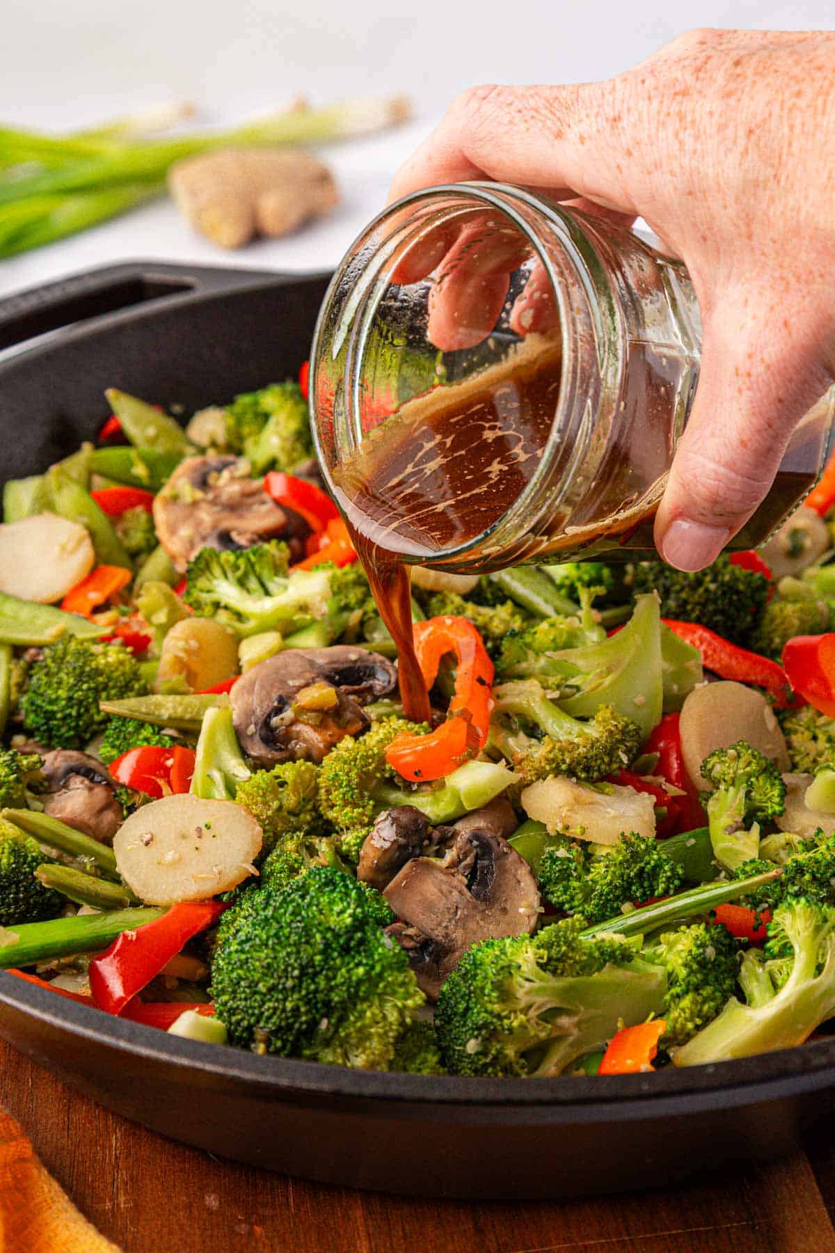 pouring stir fry sauce over vegetables