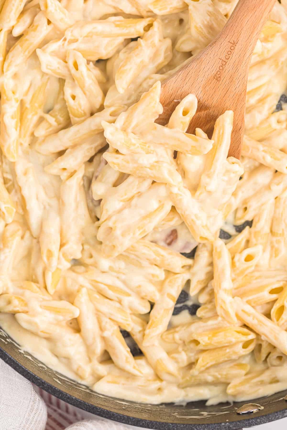 creamy penne pasta on a wooden spoon