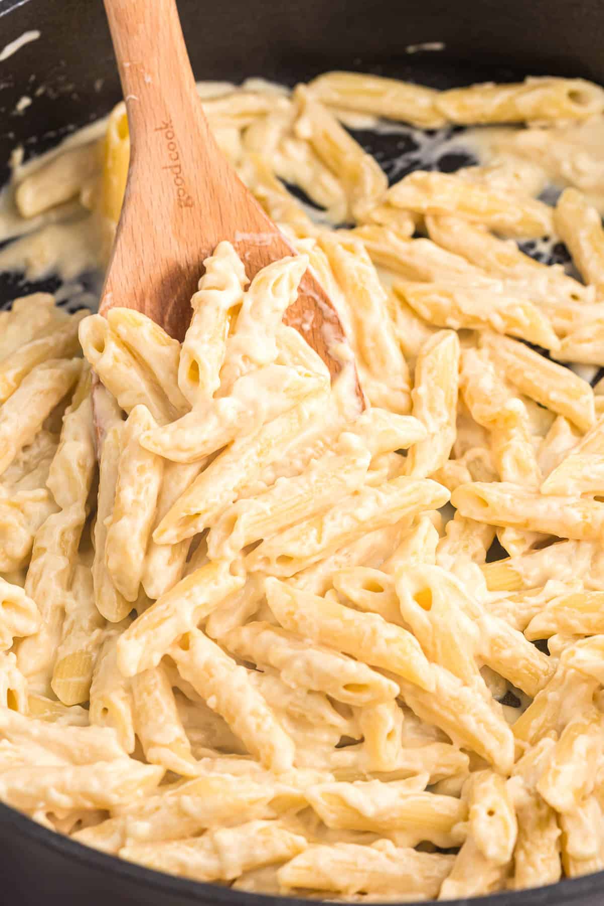 creamy penne pasta on a wooden spoon