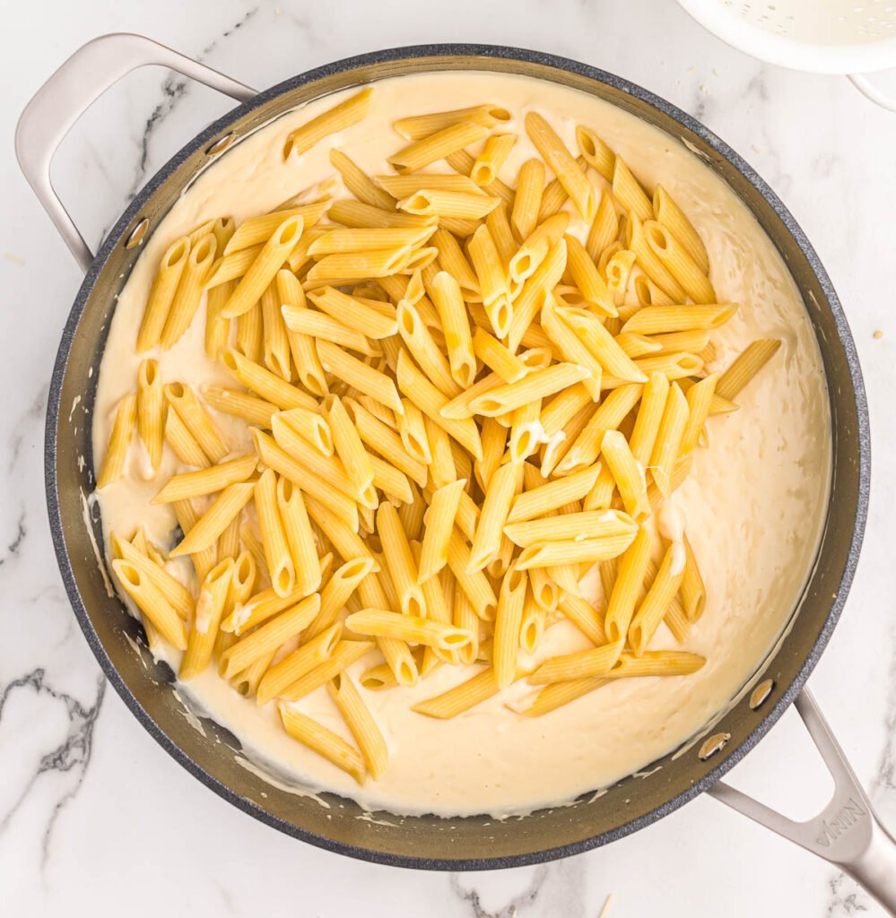 adding the penne pasta to the cream sauce