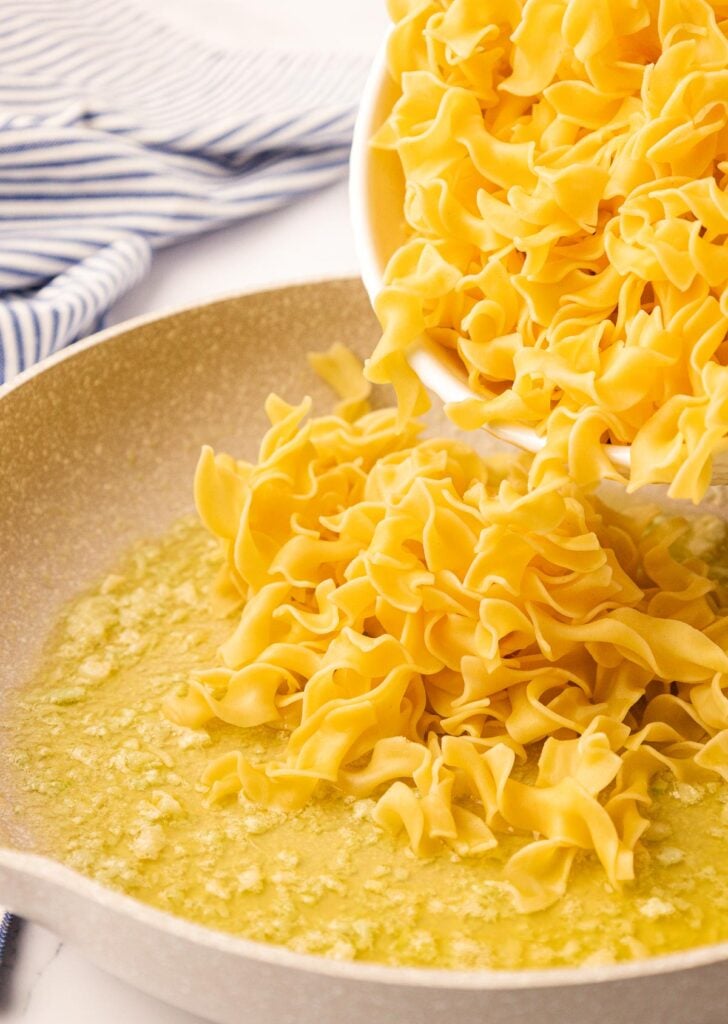 pouring egg noodles into garlic butter