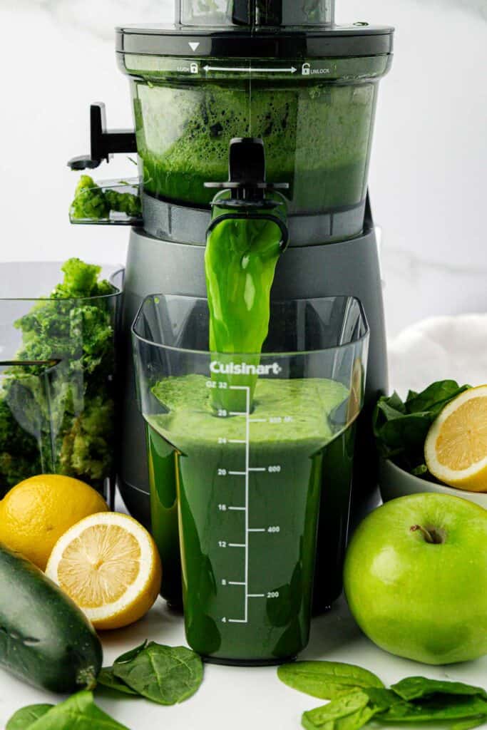 spinach juice pouring out of a juicer
