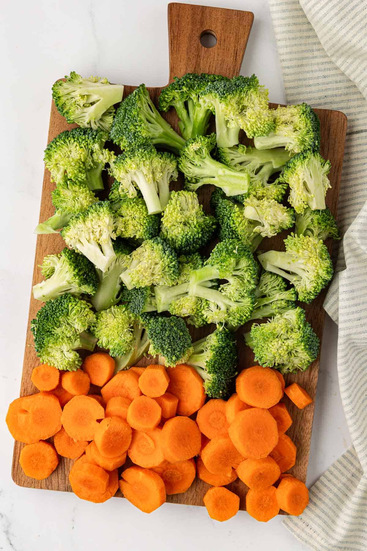 broccoli florets and sliced carrots on a wooden cutting board