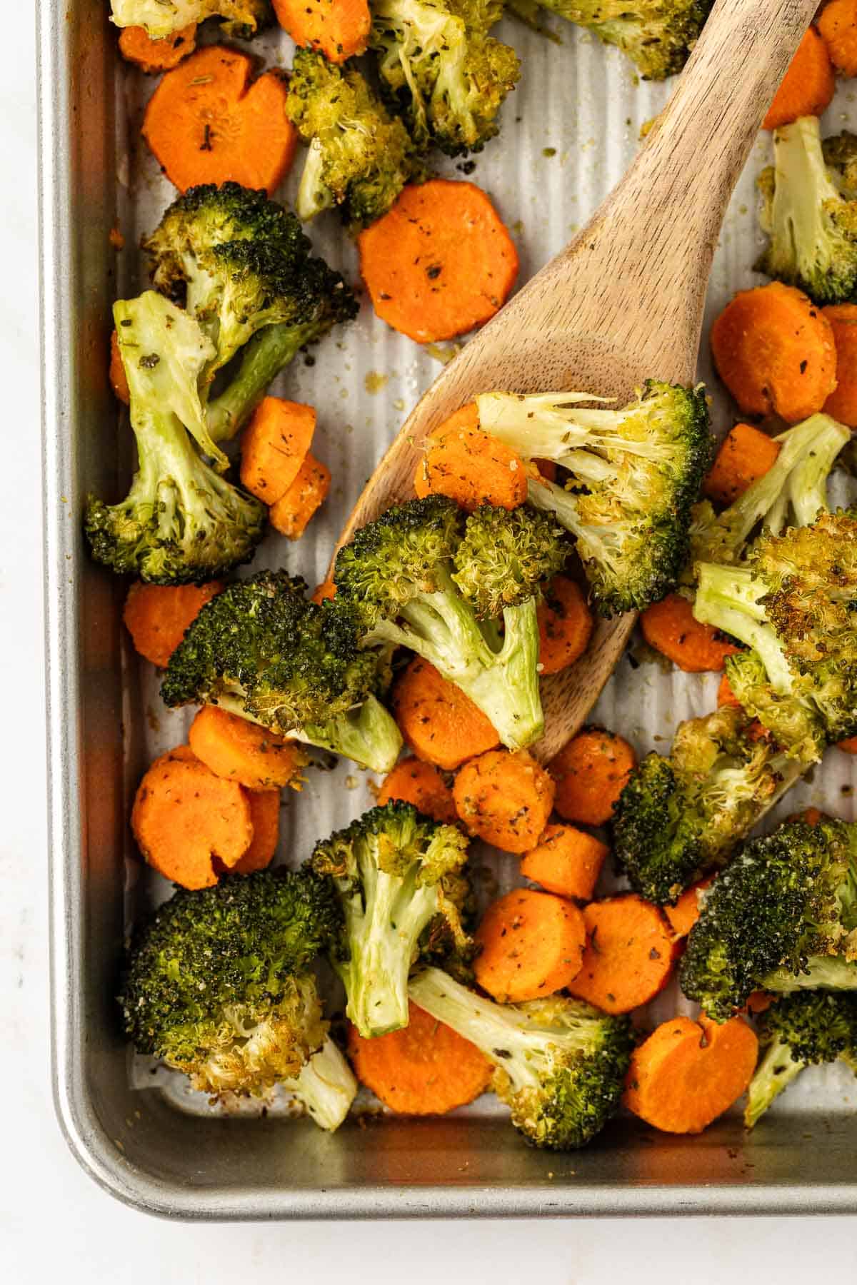 roasted broccoli and carrots on a baking sheet with a wooden spoon for serving