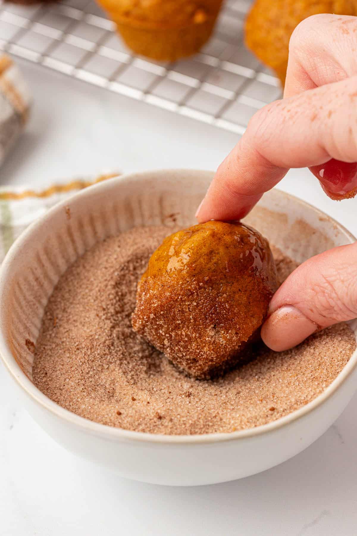 dipping a pumpkin mini muffin into cinnamon sugar