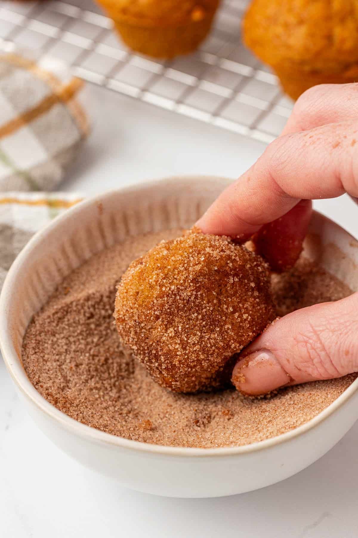dipping a pumpkin mini muffin into cinnamon sugar