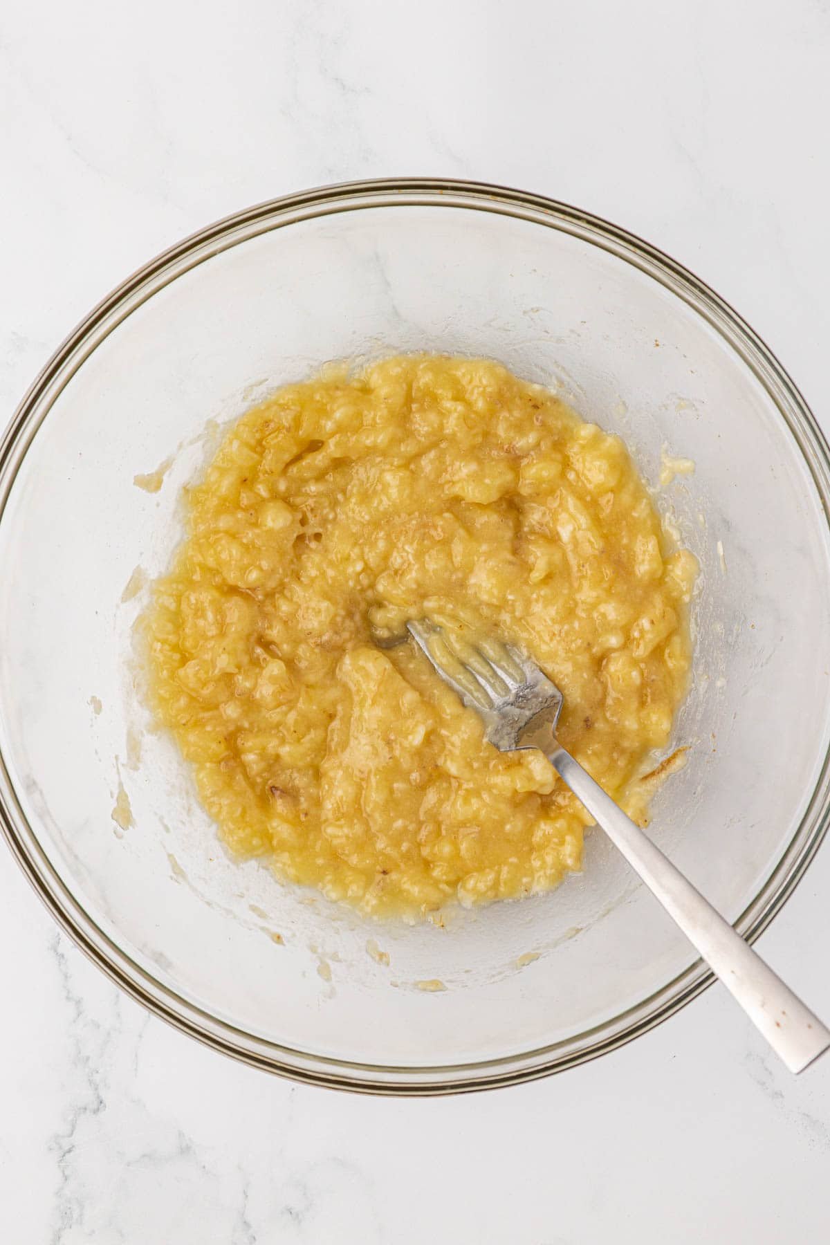 mashed bananas with a fork in a mixing bowl