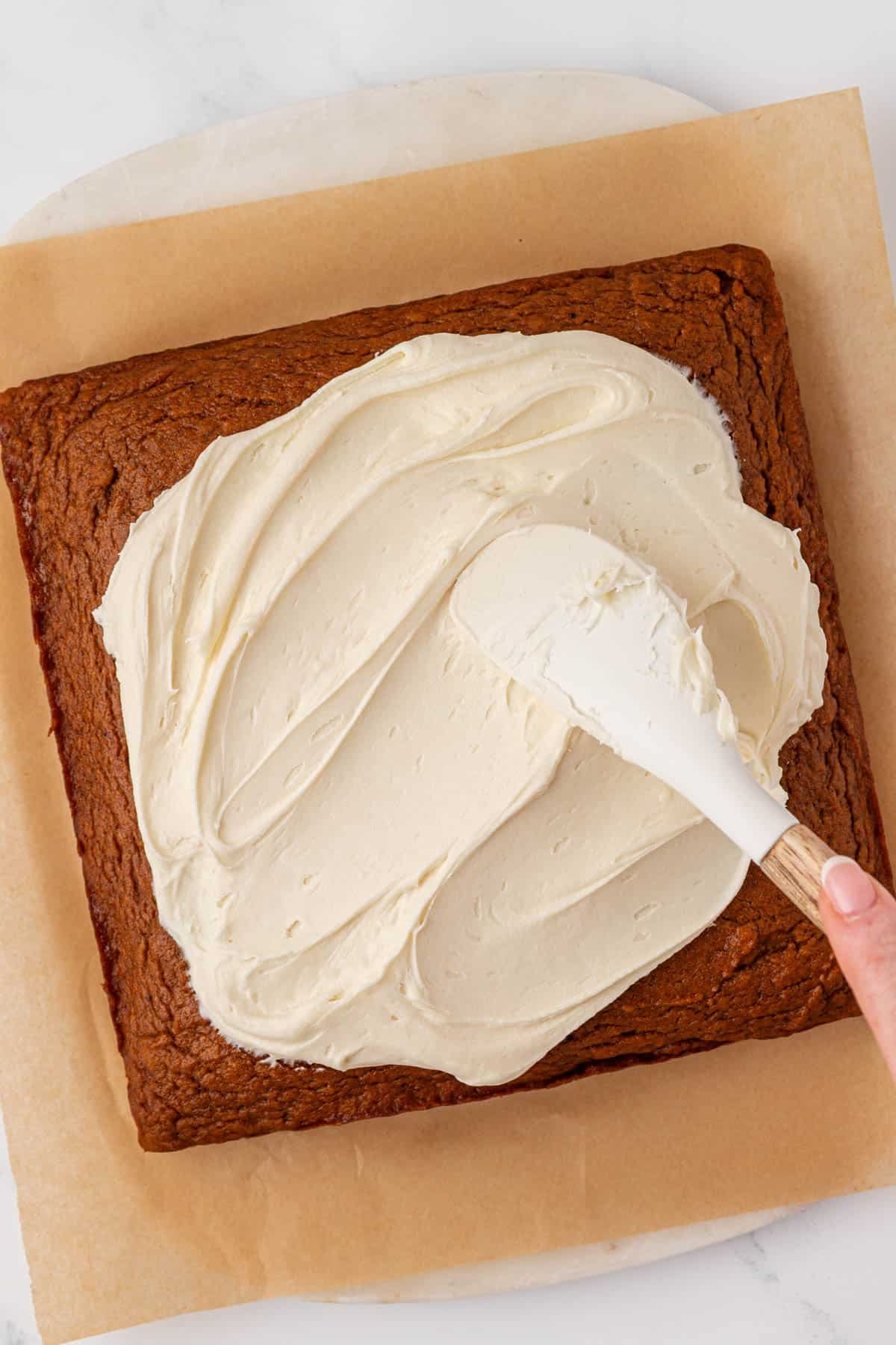 spreading the cream cheese frosting onto the pumpkin cake