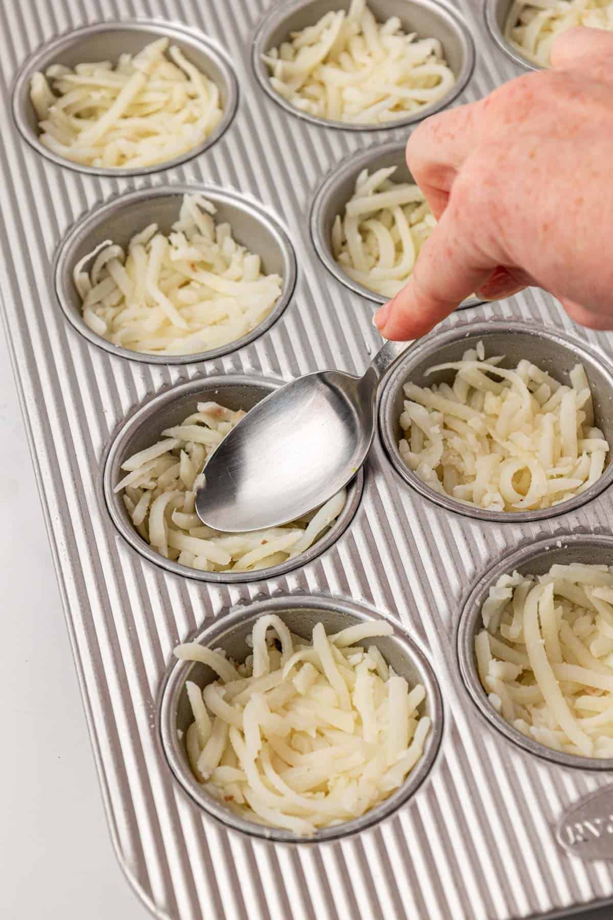using a spoon to press hash browns into a muffin tin