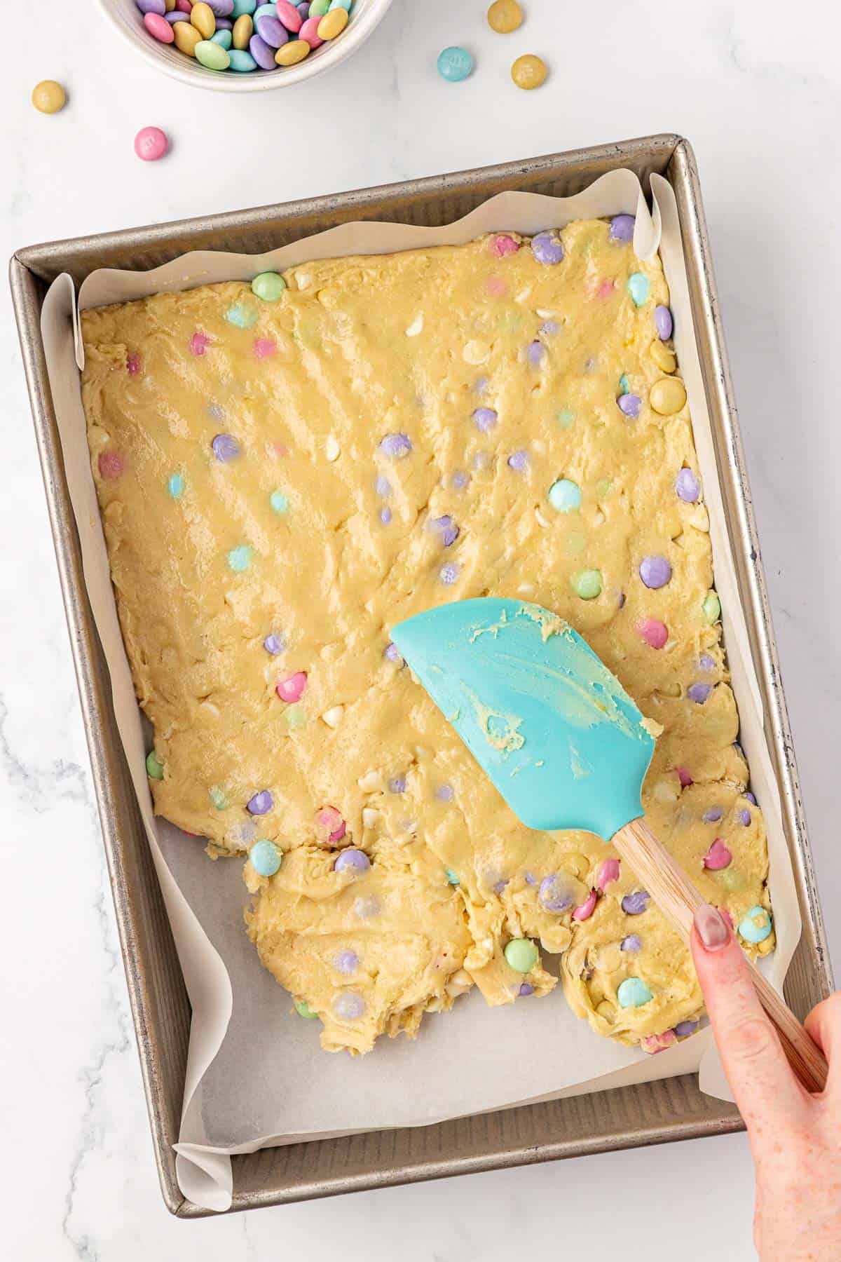 Pressing the cookie batter into the baking dish with a rubber spatula