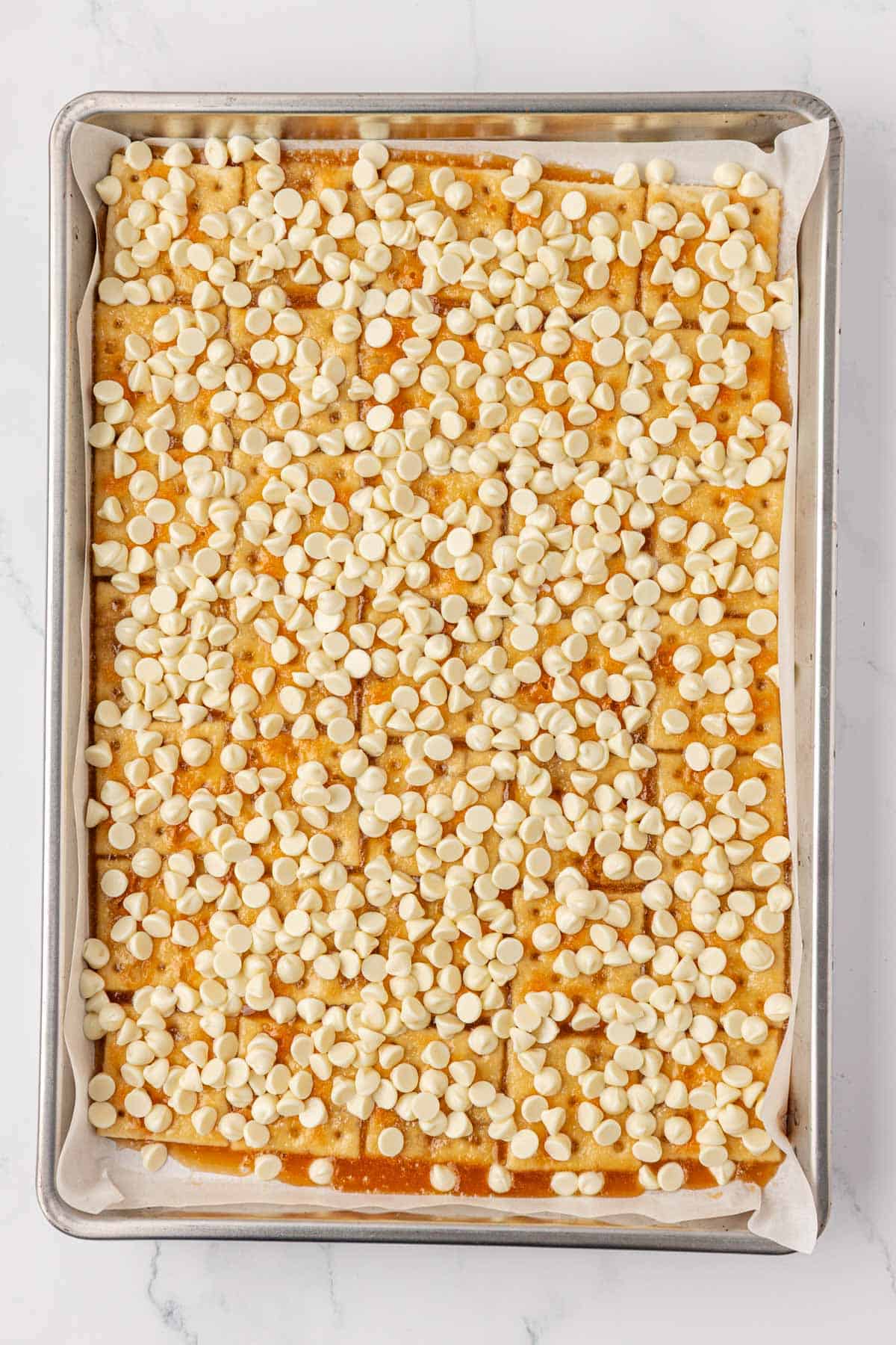 white chocolate chips on top of saltine toffee crackers