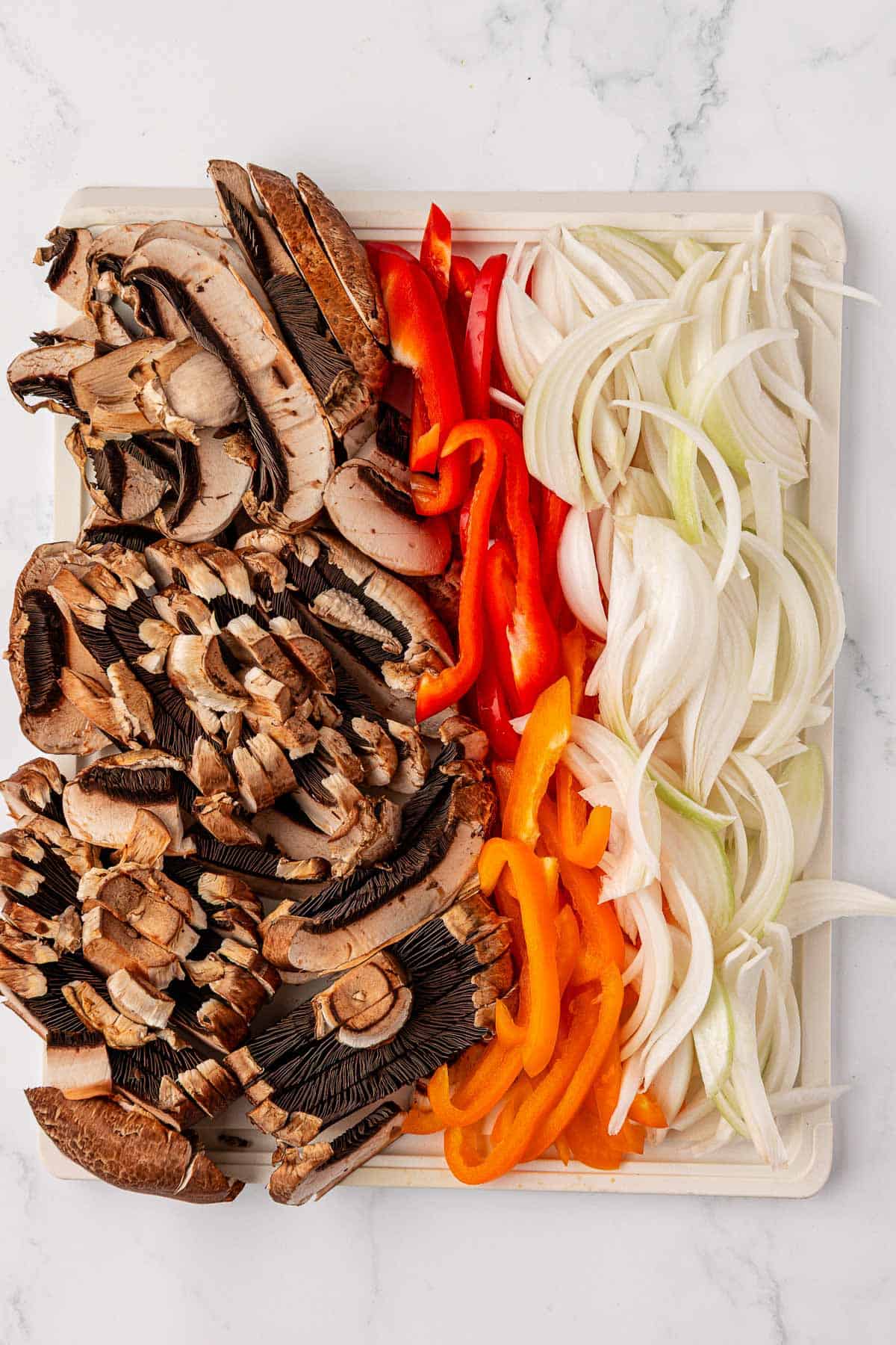 sliced portobello mushrooms, bell peppers, and onions on a sheet pan