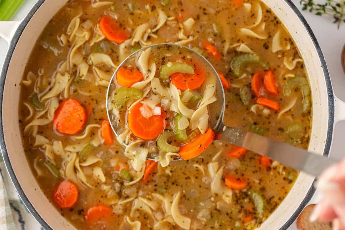 a ladle scooping vegetable noodle soup from a pot