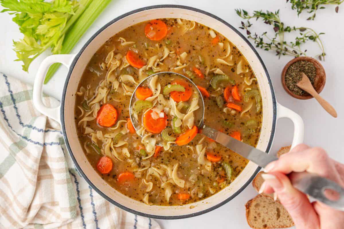 a ladle scooping vegetable noodle soup from a pot