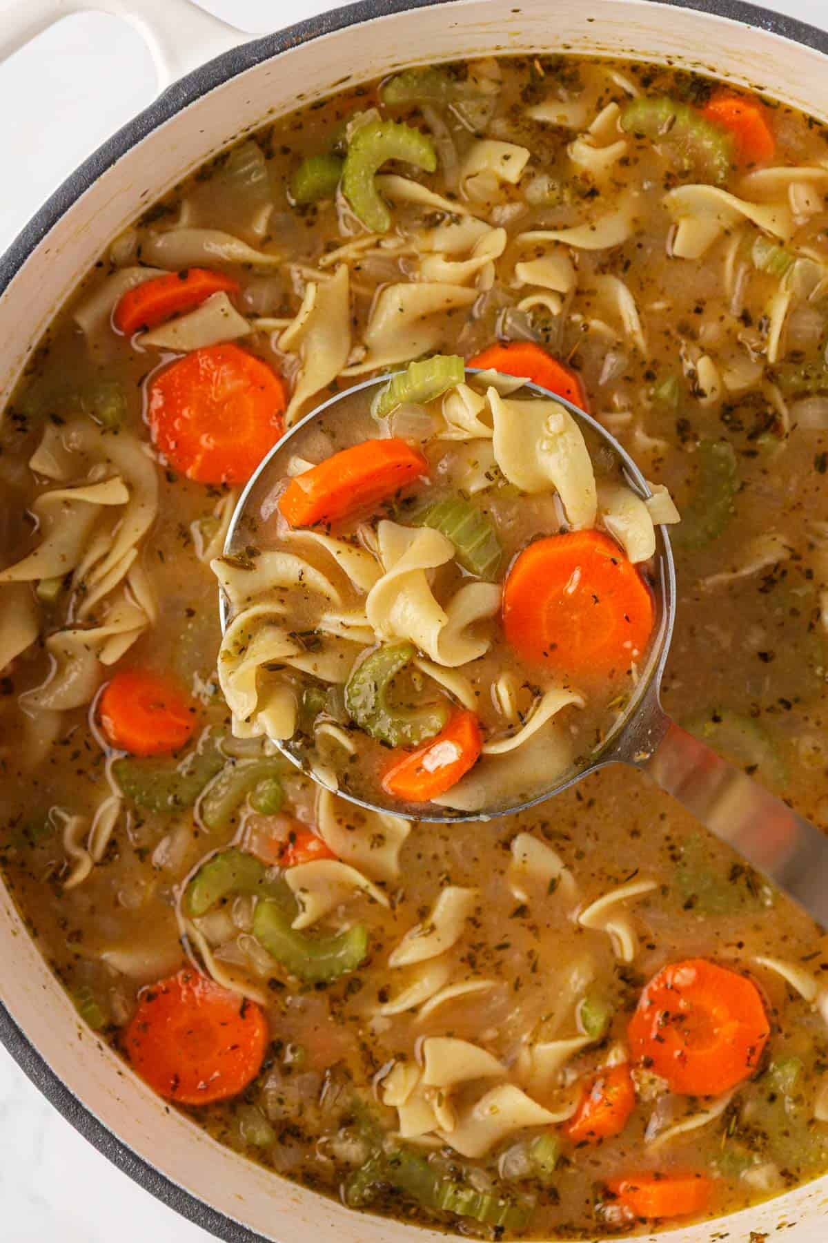 a ladle scooping vegetable noodle soup from a pot