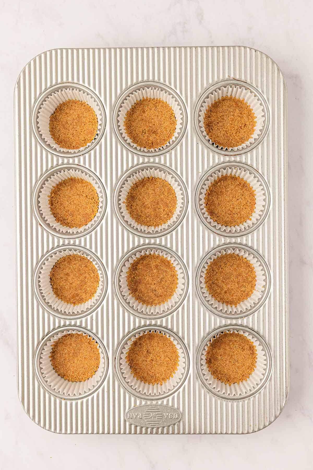 graham cracker crust pressed down into lined muffin tins